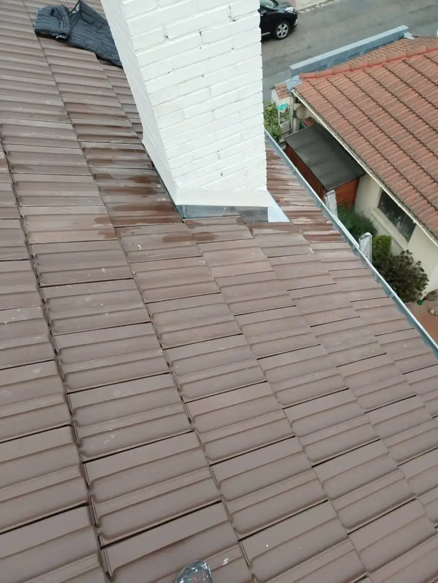 Souche de cheminée blanche sur une toiture en tuiles brunes, avec un raccord en zinc usé à sa base