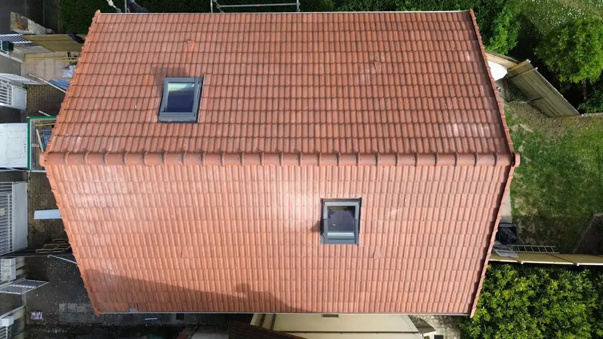 Vue de drone de la même toiture refaite en tuiles mécaniques rouges neuves, avec ses fenêtres de toit neuves